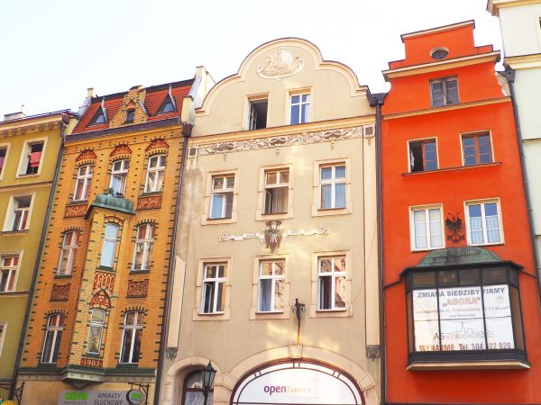 fasady kamienic pięknie odnowione, zachwycają prezencją - n/z po prawej  balkon obudowany a nad nim herb kuty, po lewej : piętrowy wykusz z ozdobną elewacją i n