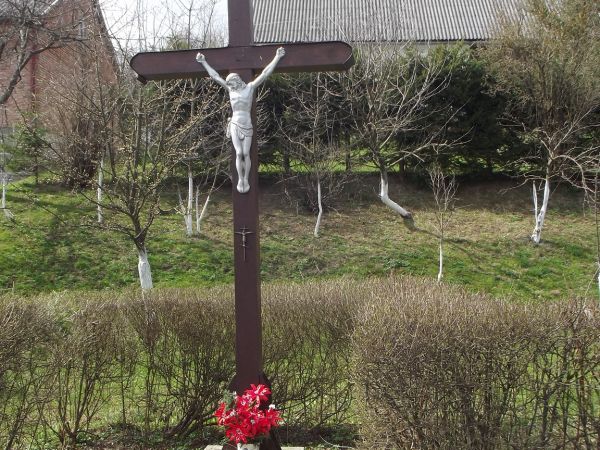 przy drodze : krzyż drewniany z wizerunkiem Chrystusa - wyraz czci i chwały Najwyższemu - tu : rzymsko-katolicki  a poniżej na belce : zawieszony krzyż metalowy