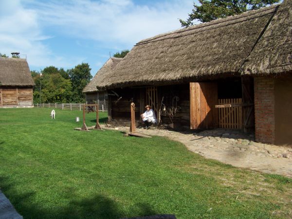 Chłop odpoczywa w cieniu wiejskich zabudowań.