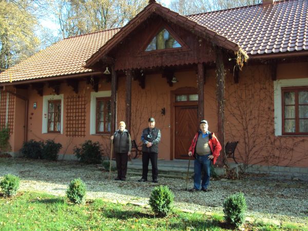 przed budynkiem dawnego folwarku - "na Chmurówkach". Budynek zbudowany z cegły, z artystycznie wykonanymi drewnianymi słupami, zakończeniami krokwi, drzwi, okie
