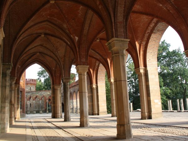 pałacowe podcienia arkadowe, dalej jedna baszta wzbogacona o krenele - tj. prostokątne występy wieńczące mury i baszty obronne, stanowiące osłonę dla strzelając