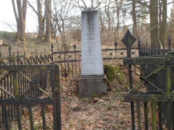 obelisk nagrobny przed dużą mogiłą, otoczony misternie wykonanym kutym płotem - na cmentarzu ewangelickim.