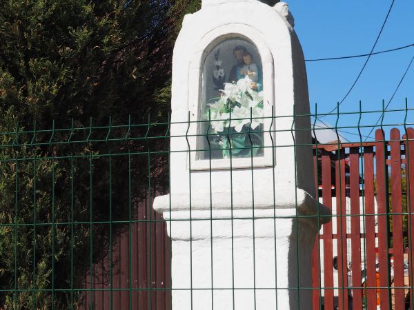 kapliczka przydrożna, zabytkowa, w niszy : figura przedstawiająca św. Antoniego z Padwy z Dzieciątkiem, przy prawej ręce lelija /lilija/, święty pomaga podczas