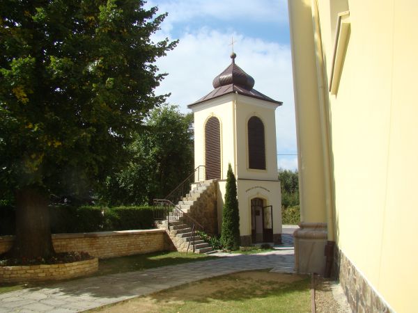 dzwonnica murowana z kamienia, dzwon z 1760r., dach namiotowy z kopułką ośmioboczną zakończoną krzyżem, zewnątrz - schody na piętro a tam czterema arkadami prze