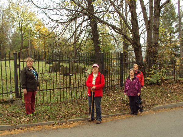 przy bramie cmentarnej - na niej "Gwiazdy Dawida", dalej: kirkut żydowski a na nim macewy - płyty nagrobne. Szalom - hebr pokój, słowo używane przez Żydów jako