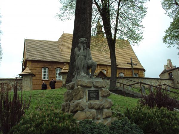 pięknie odnowiony modrzewiowy zabytkowy kościół - podniesiony do godności Sanktuarium Dzieciątka Jezus, tu n/z rzeźba Chrystusa Frasobliwego na cokole kamiennym