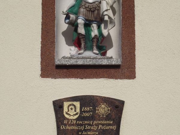 fronton remizy strażackiej - tam : tablica w intencji oraz w niszy rzeźba przedstawiająca św. Floriana z cebrzykiem z wodą - patron m.in strażaków.