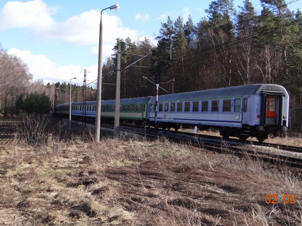Widok na miejsce po dawnym strzeżonym przejeździe kolejowym, pociąg opuszcza toty stacji jadąc w kierunku Olsztyna.
