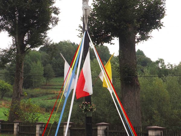 krzyż z rzeźbą Chrystusa, ludową, nakrytą pozornym daszkiem - udekorowany flagami i kolorowymi wstążkami w barwach kościelnych i narodowych.