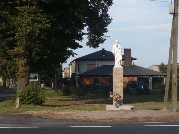 We wsi przy drodze nr 11 figura Serca Pana Jezusa i w tle droga do wsi