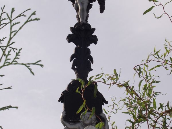 krzyż żeliwny o ubogaconej inskrypcji z medalionem - osadzony w kamiennym postumencie - zwraca uwagę odłamany kiść wici roślinnej z symetrycznej formy dekoracji