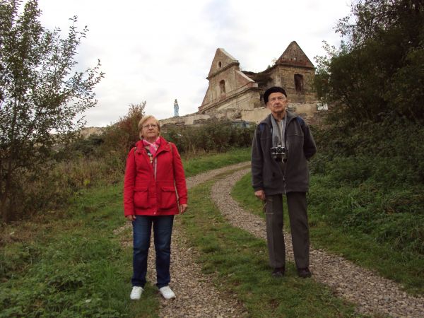 przed ruinami obronnego klasztoru Karmelitów Bosych, po lewej od kościoła na wysokim cokole figura Matki Boskiej. W kompleksie klasztornym wkrótce powstanie m.i