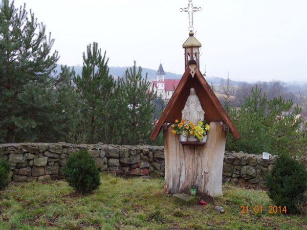 na wzgórzu cerkiewnym : kapliczka z figurką Matki Boskiej, ładna, "inna", ukwiecona, za nią widoczny stary mur okalający cerkiew. Dalej : widoczny nowy kościół.