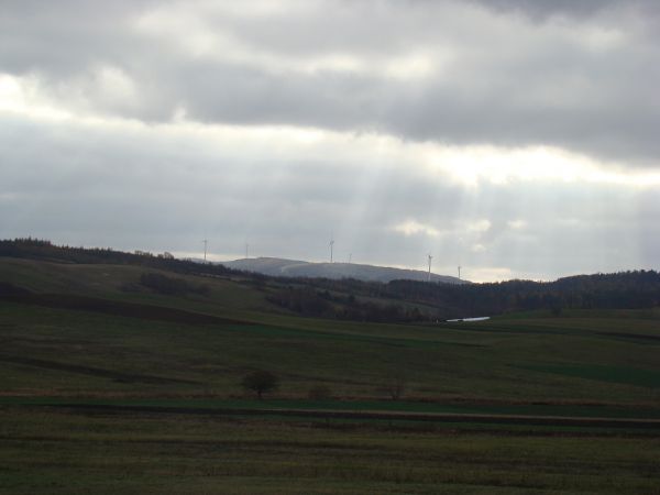 na dalszym planie: farma wiatrowa na zalesionych wzniesieniach Pogórza Bukowskiego a pamiętają niektórzy, że we wsi wydobywano węgiel brunatny, że to on stanowi