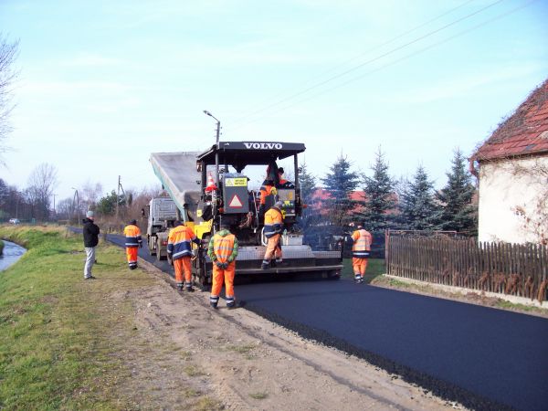 Maszyna układa nowy asfalt na drodze gminnej.