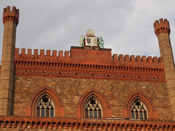 kartusz herbowy zdobny koroną - strzeżony przez lwa i rycerza, krenelaż zwieńczający fasadę zamkową - główną, reprezentacyjną i element zdobiący  i fortyfikując