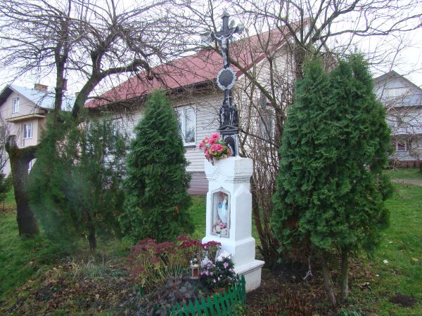 kapliczka przydrożna, zwieńczona krzyżem kutym na cokole a w nim nisza z figurą Matki Boskiej, za szkłem - jak pisał Władysław Orkan w 1922r. - zalecał, by prze