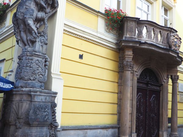 figura przedstawiająca św. Floriana, stoi na cebrzyku - służącym do noszenia wody koniecznej do gaszenia ognia,  poniżej na postumencie kartusz herbowy.