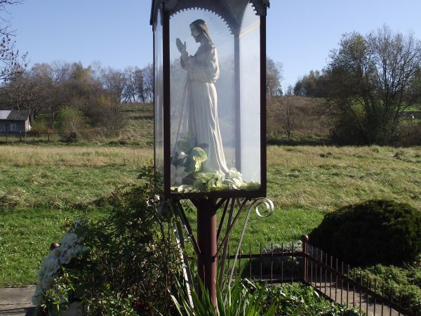 przy drodze na Bartoszów : kapliczka z figurą Chrystusa, stylowa, oszklona,  pokryta blachą - zwieńczona krzyżem osadzonym w makowiczce, otoczona płotkiem, zadb