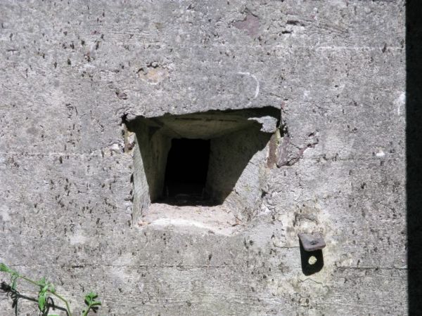 Jeden z dwóch otworów strzelniczych stanowiska obrony wejścia do Schronu nr 2. w Dobieszewku. Na prawo widoczna metalowa sztaba zamykająca drzwi, bądż kratę pan