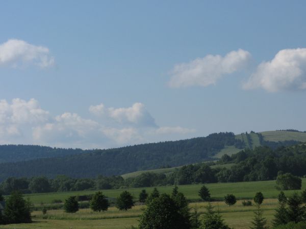 kapliczka przydrożna - na dole zdjęcia po lewej a dalej zalesione wzgórza i po prawej wyciąg narciarski.