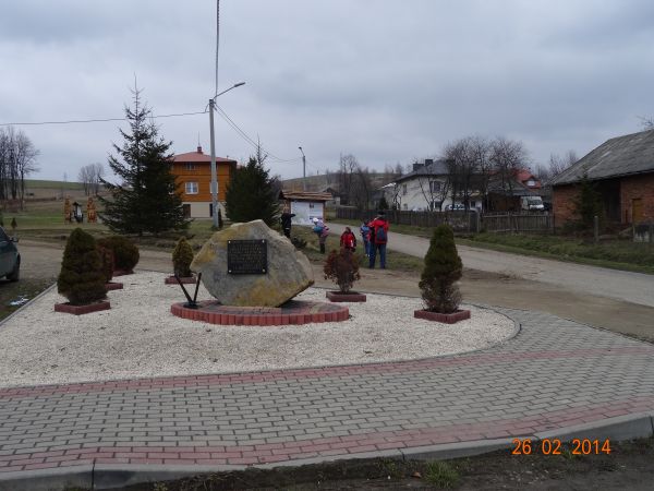 w centrum wsi - j/w., powyżej po lewej : działo / armata i wojowie / artylerzyści  a wyżej fragment obsadzonego parkiem cmentarza.