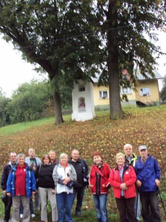 przed wiejską kapliczką, murowaną, pewnie zabytkową, na planie kwadratu, dwukondygnacyjną - no i zadbaną, ukwieconą, pejzaż, oko i serce radującą.