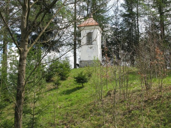 kapliczka przydrożna, przypotokowa, wzniesiona w XVIII wieku na wzgórku przy skrzyżowaniu dróg, dwukondygnacyjna na cokole, górna kondygnacja przepruta z trzech