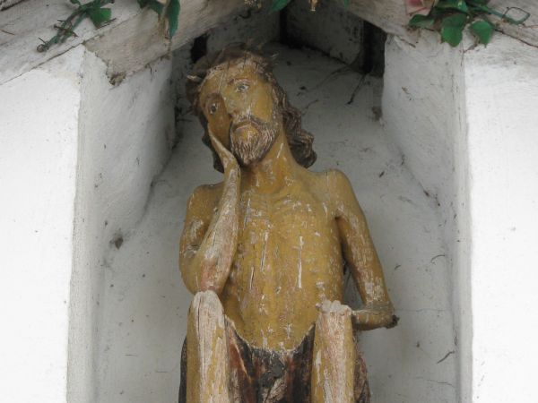 w płycinie kapliczki, nad wejściem: figurka /rzeźba ludowa/ Chrystusa Frasobliwego, którego wizerunek kojarzy się głównie z biedą otoczenia, ale jednocześnie z