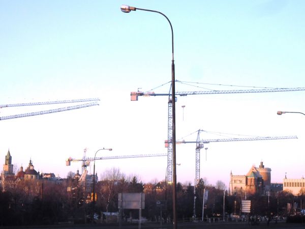 HISTORIA I TERAŹNIEJSZOŚĆ. W tle budynki i wieże lubelskiej Starówki oraz Zamek. Na pierwszym planie, żurawie budowlane na budowie centrum handlowego.