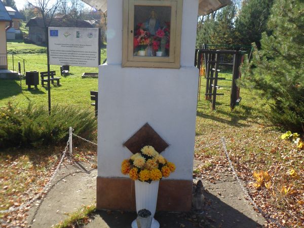 kapliczka przydrożna z figurką Matki Bożej w oszklonej niszy - zabytkowa,  ukwiecona, zadbana.