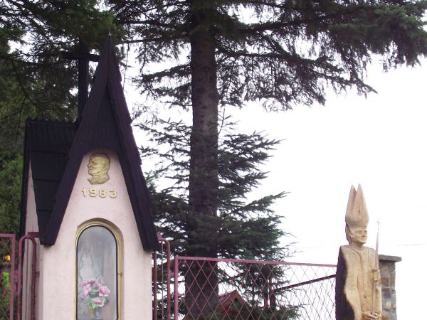 współczesna przydomowa kapliczka z figurą Matki Boskiej i inskrypcją wotywną, przed: rzeźba przedstawiająca papieża J.P. II - pomnik wotywny upamiętniający 2-gą