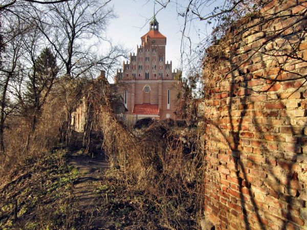 Reszel,fragment muru obronnego średniowiecznego otaczającego Stare Miasto między zamkiem a Starą Plebanią,widok od strony parku miejskiego,w głębi kościół gotyc