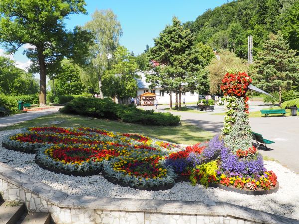 przy deptaku - w ciągu spacerowym pięknie nasadzony skwer kwiatowy , dalej niedźwiadek przy ławkach , centralnie pomnik źródeł a po lewej "Zielony Domek".