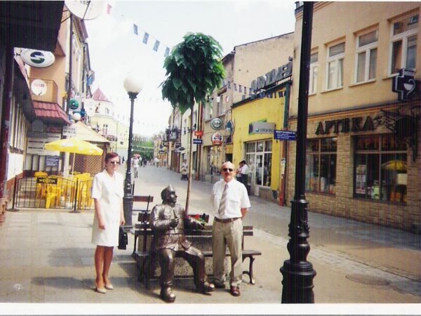 przed/obok pomnika - ławeczki z wojakiem Szwejkiem - odsłoniętym 6 czerwca  2003r. m.in. przez wnuka Jarosława Haszka, Richarda Haszka. Dalej po lewej : pergola