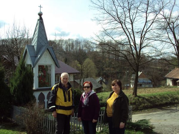 przy / obok kapliczki, przydomowej, współczesnej - ogrodzonej płotkiem, zadbanej i ukwieconej, o ciekawej, stylowej bryle i uposażeniu. Kapliczka rodziny Ściera
