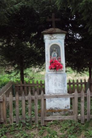 kapliczka przydrożna, otoczona drewnianym płotkiem, murowana, zabytkowa, znak obecności chrześcijaństwa i ludowej pobożności.