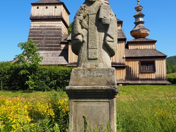 kamienna figura św. Mikołaja - przed drewnianą cerkwią św. św. Kosmy  i Damiana, na bazie cokołu czytelna inskrypcja wyryta w materii kamienia - słowa pisane az