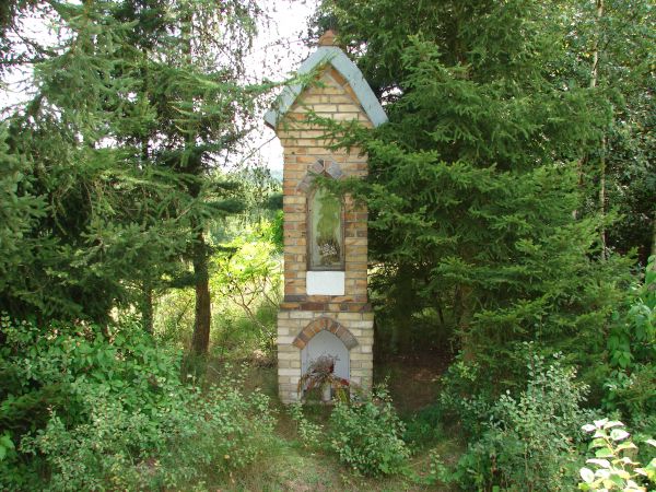 Przydrożna figurka,murowana,we wnęce porcelanowa postać Matki Boskiej z Dzieciątkiem.