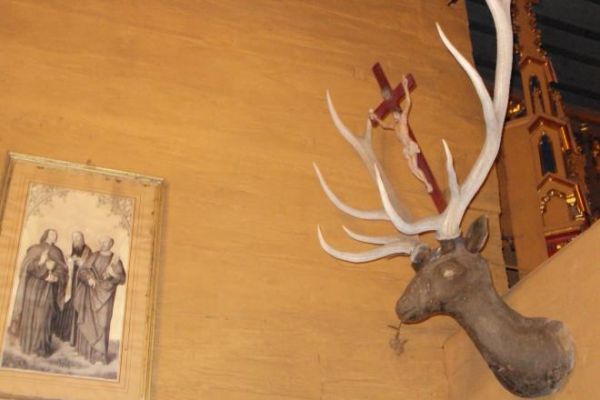 przed głównym ołtarzem, w prezbiterium - zawieszone są na belce tęczowej wota i tu n/z rzeźbiona w drzewie głowa jelenia z krzyżem między rogami - to ze sceny o