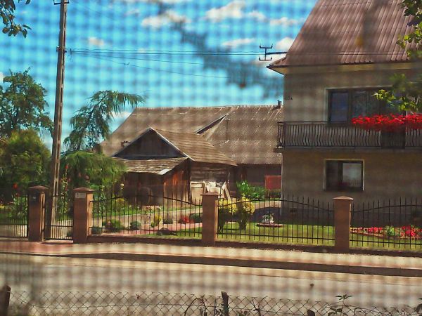 Widok na ulicę przez firankę w oknie.