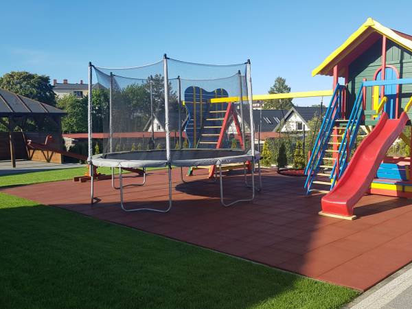 Plac zabaw z widokiem na altanę grilową wyposażoną w meble piknikowe oraz grille