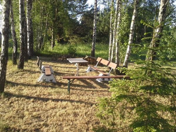 Ławeczki i stoliki przy palenisku usytuowane w dalszej części posesji