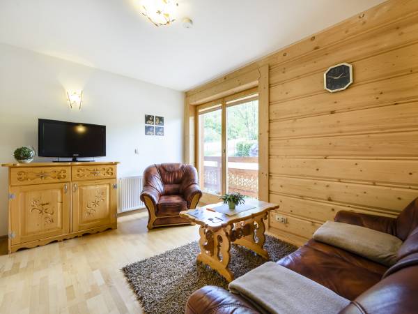 nieduży salon z kanapą skórzaną i fotelem oraz wyjściem na balkon